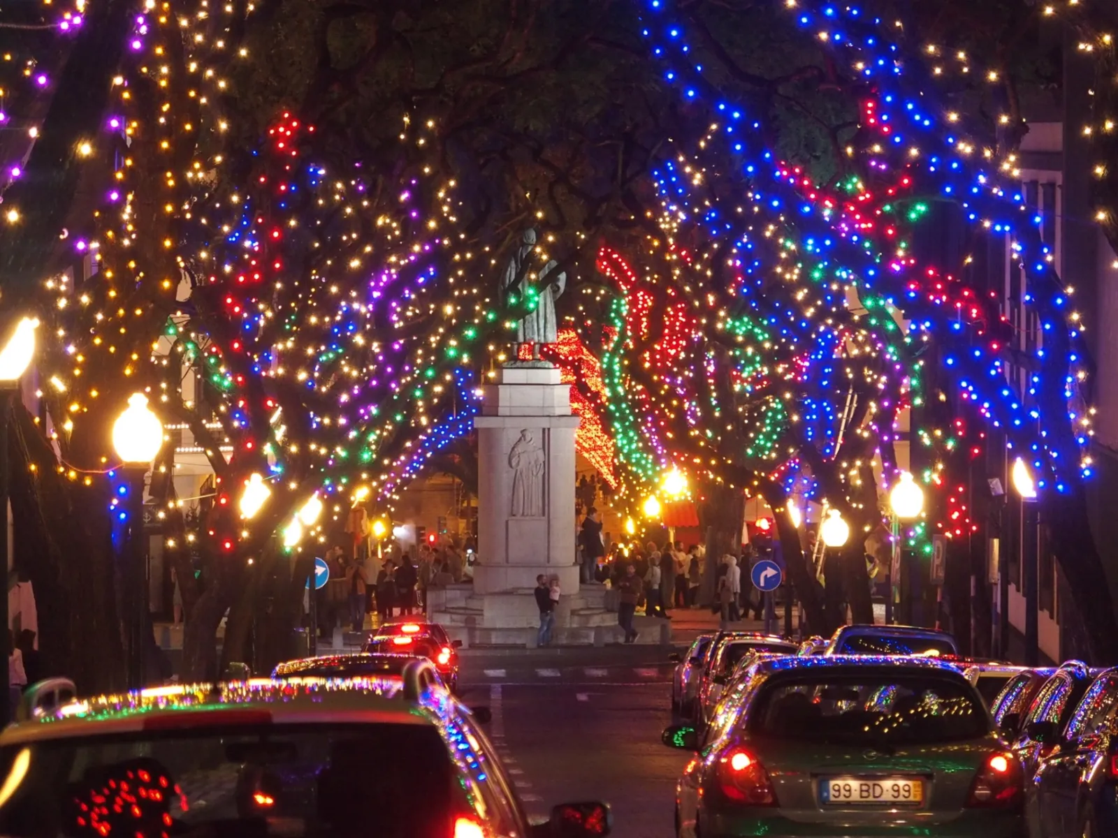 Avenida Arriaga in Funchal covered in dense, colourful Christmas lights, with trees and cars decorated for the festive season