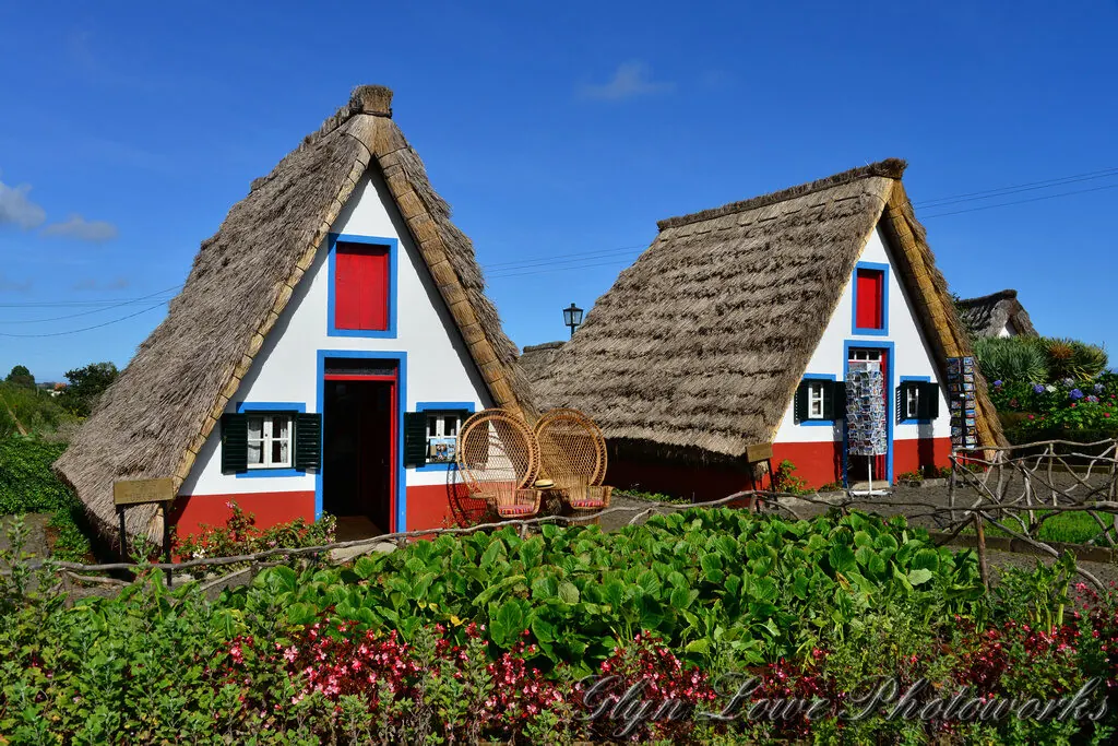 Casas típicas de Santana na Madeira — pequenas casas triangulares de colmo pintadas de branco, vermelho e azul, rodeadas por jardins floridos